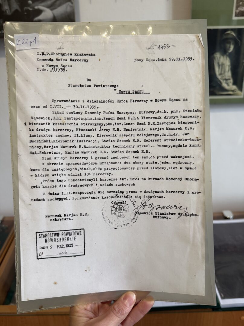 Typed Polish document with stamps, held in a clear plastic sleeve by a person.
