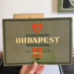 Hand holding a vintage poster that reads 'JAMBOREE BUDAPEST HUNGARIA 1933' with a red heart emblem and crest.