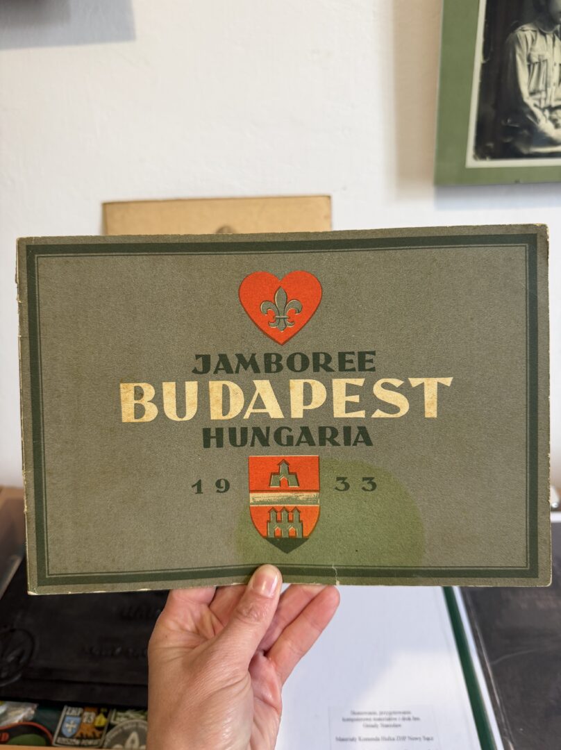 Hand holding a vintage poster that reads 'JAMBOREE BUDAPEST HUNGARIA 1933' with a red heart emblem and crest.