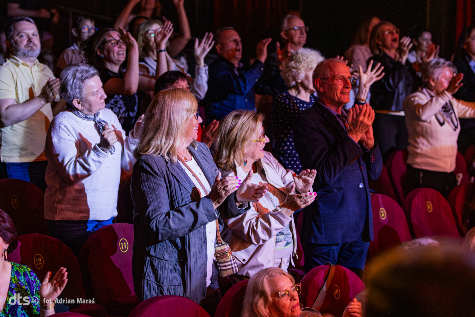 Audience members standing and clapping in a theater during a performance.