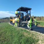 Road construction crew smoothing new asphalt on a rural road with a paver.