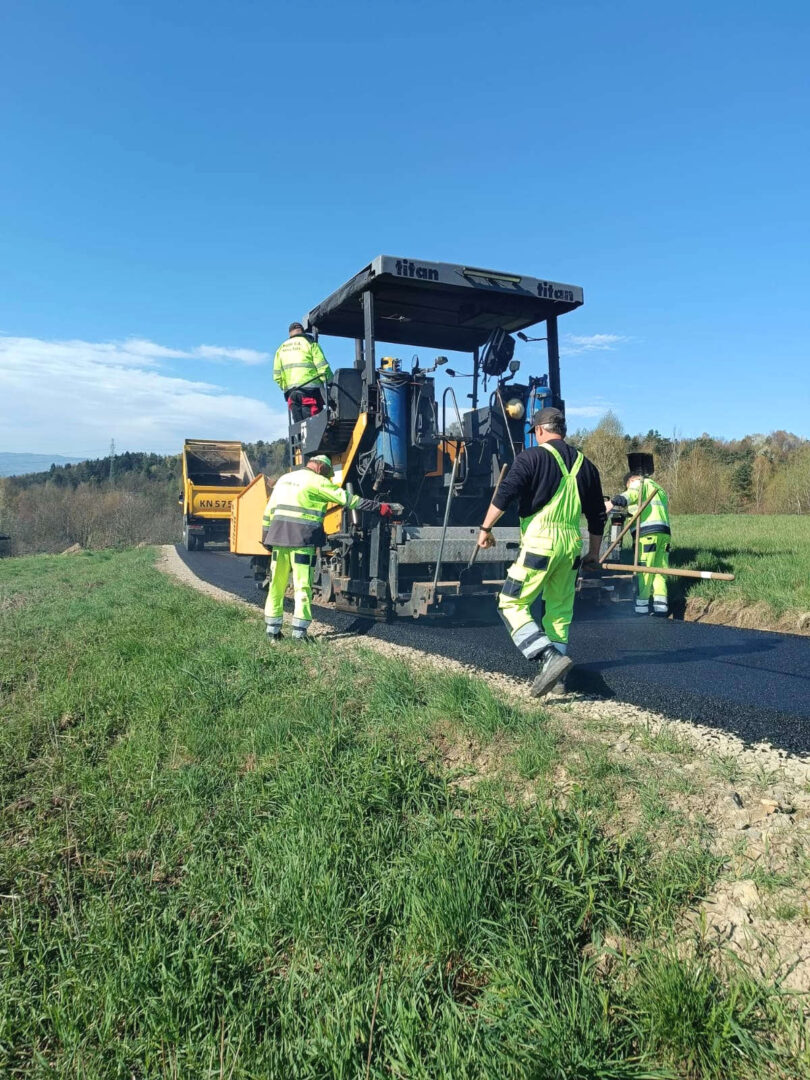 Road construction crew smoothing new asphalt on a rural road with a paver.