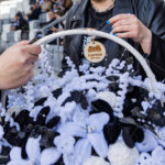Hands shaping a white-and-blue floral basket, with a round CAPOW tag, at a stadium event. (informative)