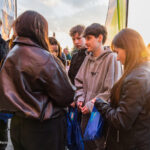 Group of teens standing in a circle outdoors at sunset, exchanging blue drawstring bags during an event.