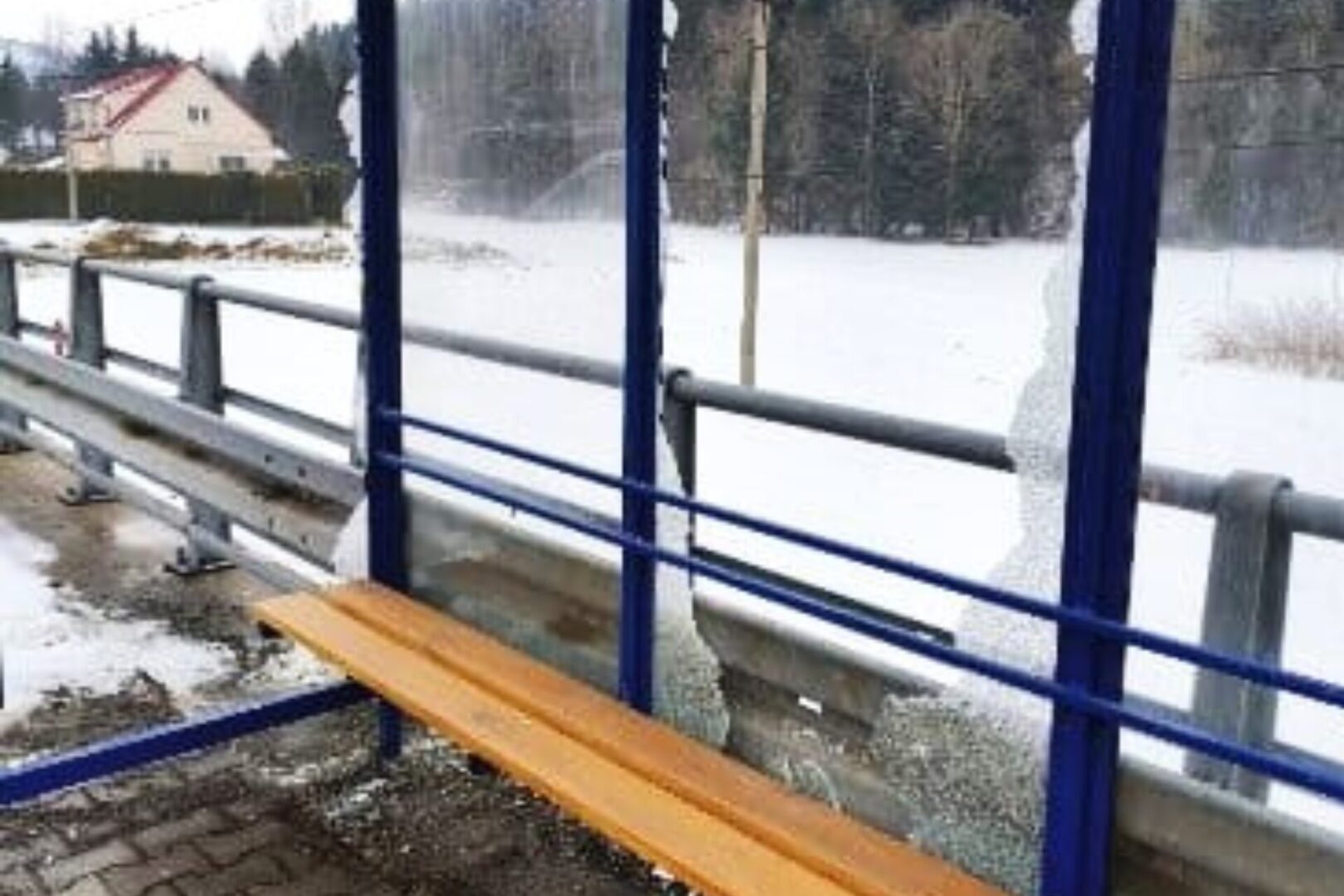 Snow-covered walkway with a broken blue railing and an orange wooden bench leaning against it.