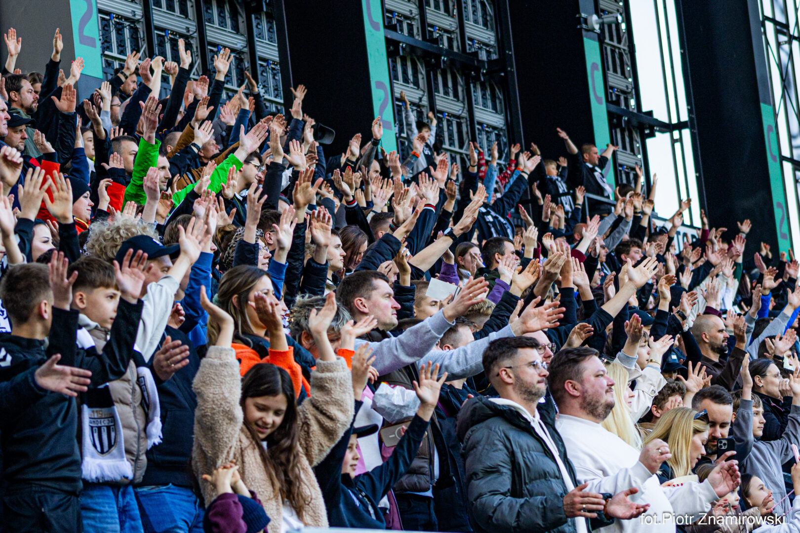 Crowd of spectators in a stadium with many hands raised in the air, cheering for a live event.