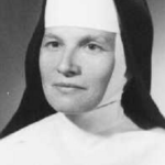 Portrait of a Catholic nun in a white wimple and black veil, looking at the camera.