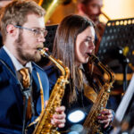 Two saxophonists in navy suits performing in a concert, focused on their sheet music.