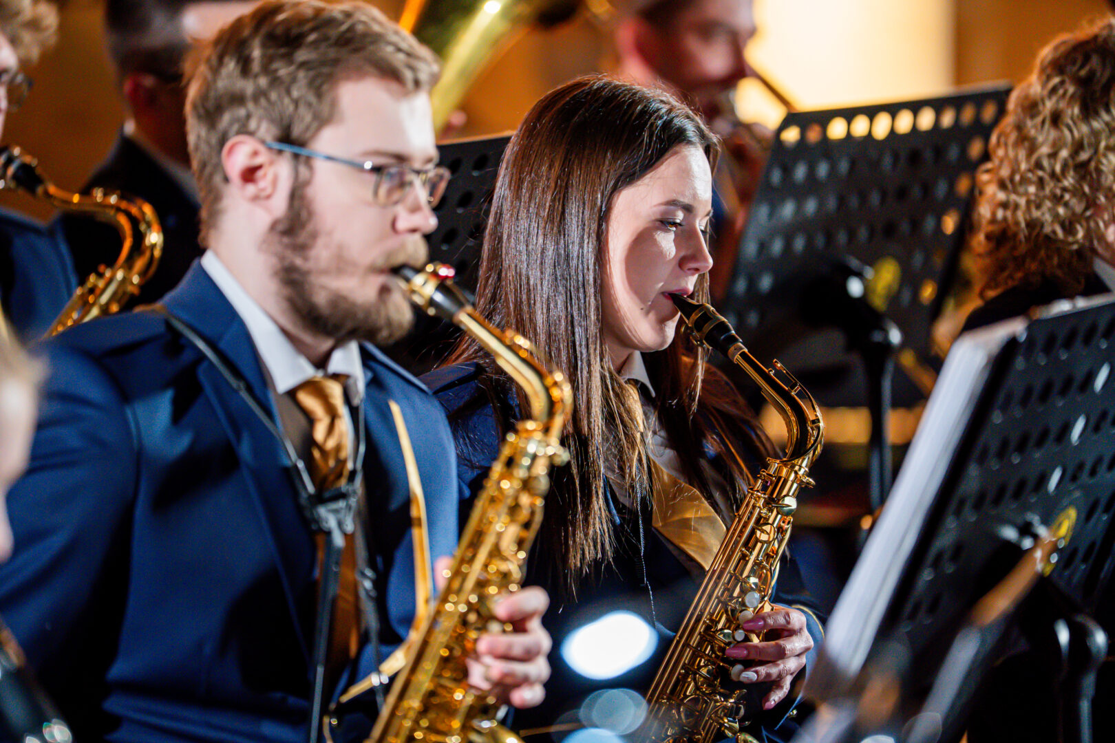 Two saxophonists in navy suits performing in a concert, focused on their sheet music.