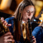 Woman in a blue uniform with a gold tie playing a clarinet in a live band performance