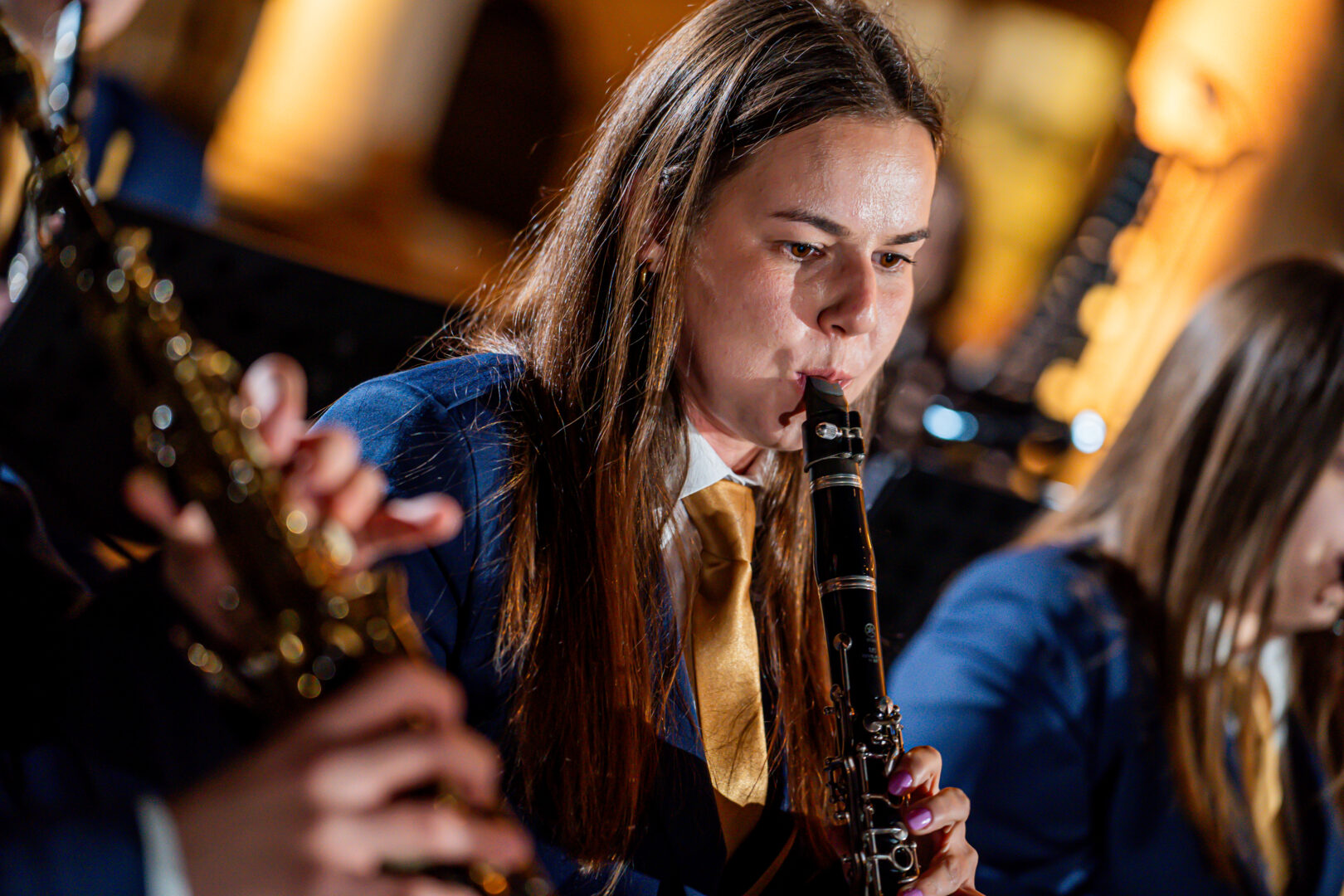 Woman in a blue uniform with a gold tie playing a clarinet in a live band performance