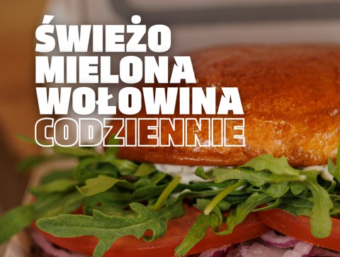 Close-up of a burger with arugula and tomato, overlaid with bold Polish text advertising 'ŚWIEŻO MIELONA WOŁOWINA CODZIENNIE' (daily fresh ground beef).