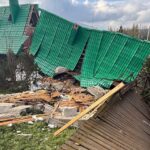 Collapsed building with a green tiled roof toppled onto rubble and wooden beams in a grassy area