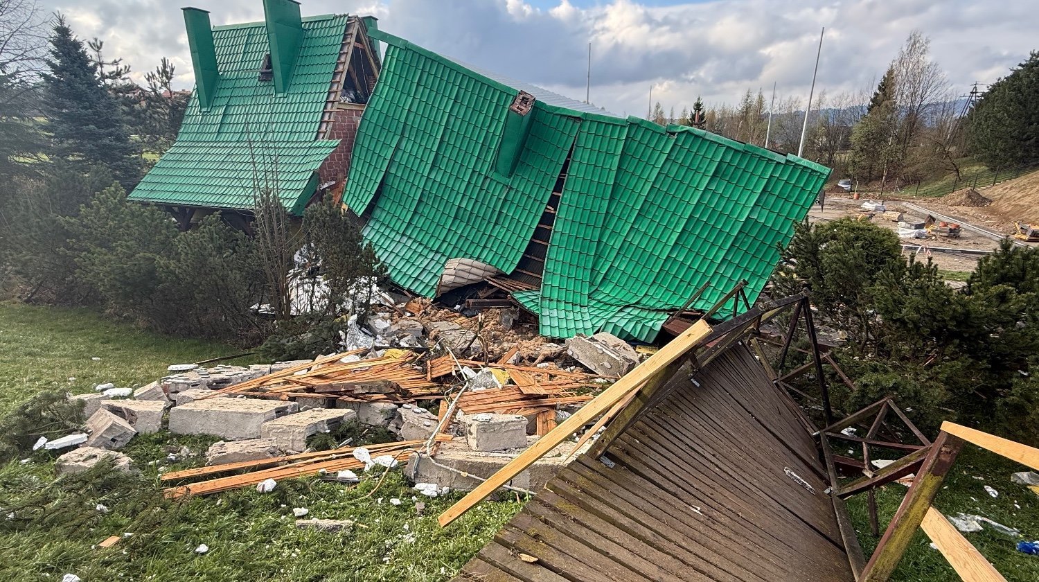 Collapsed building with a green tiled roof toppled onto rubble and wooden beams in a grassy area