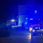 Night street with blue emergency lights and several vehicles, including an ambulance and police cars, parked along the road.