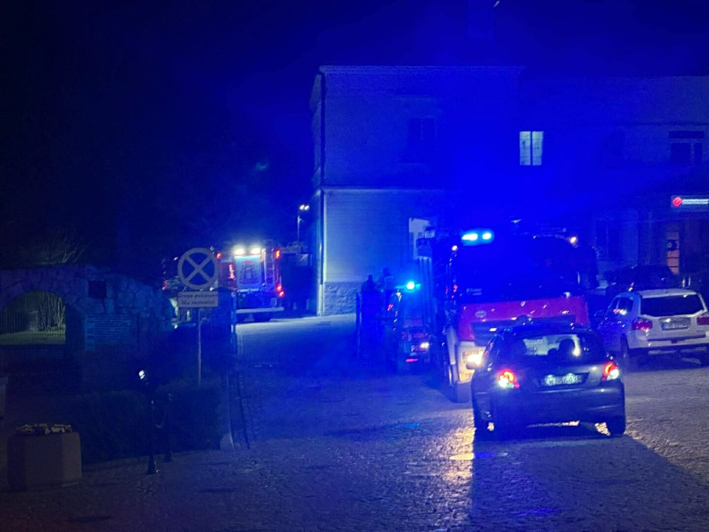 Night street with blue emergency lights and several vehicles, including an ambulance and police cars, parked along the road.