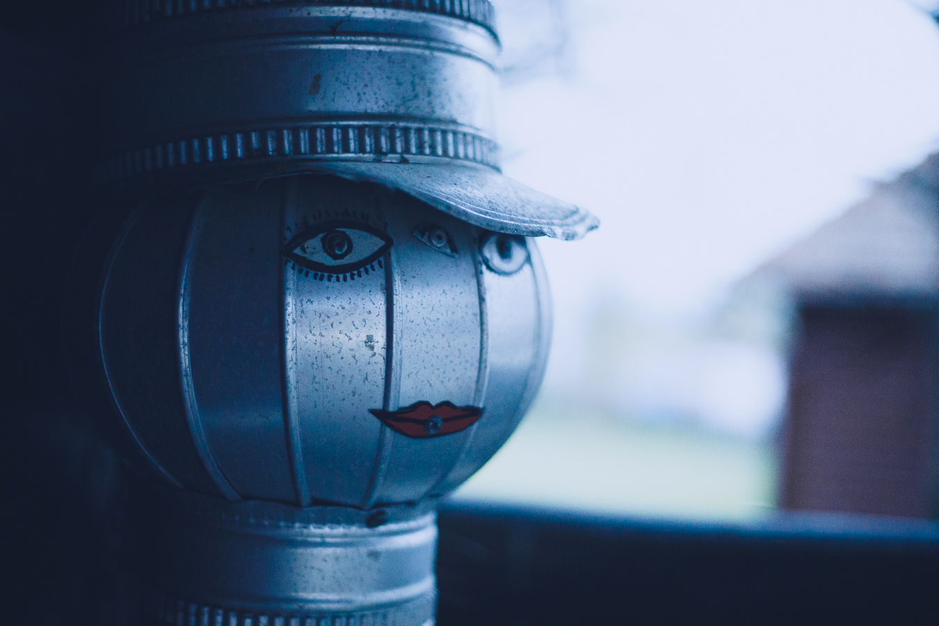 Close-up of a weathered metal lantern shaped as a face with a cap and red lips, front view in blue-tinted light.