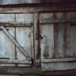 Weathered wooden double doors with a diagonal cross brace on the left door and black hinge hardware.