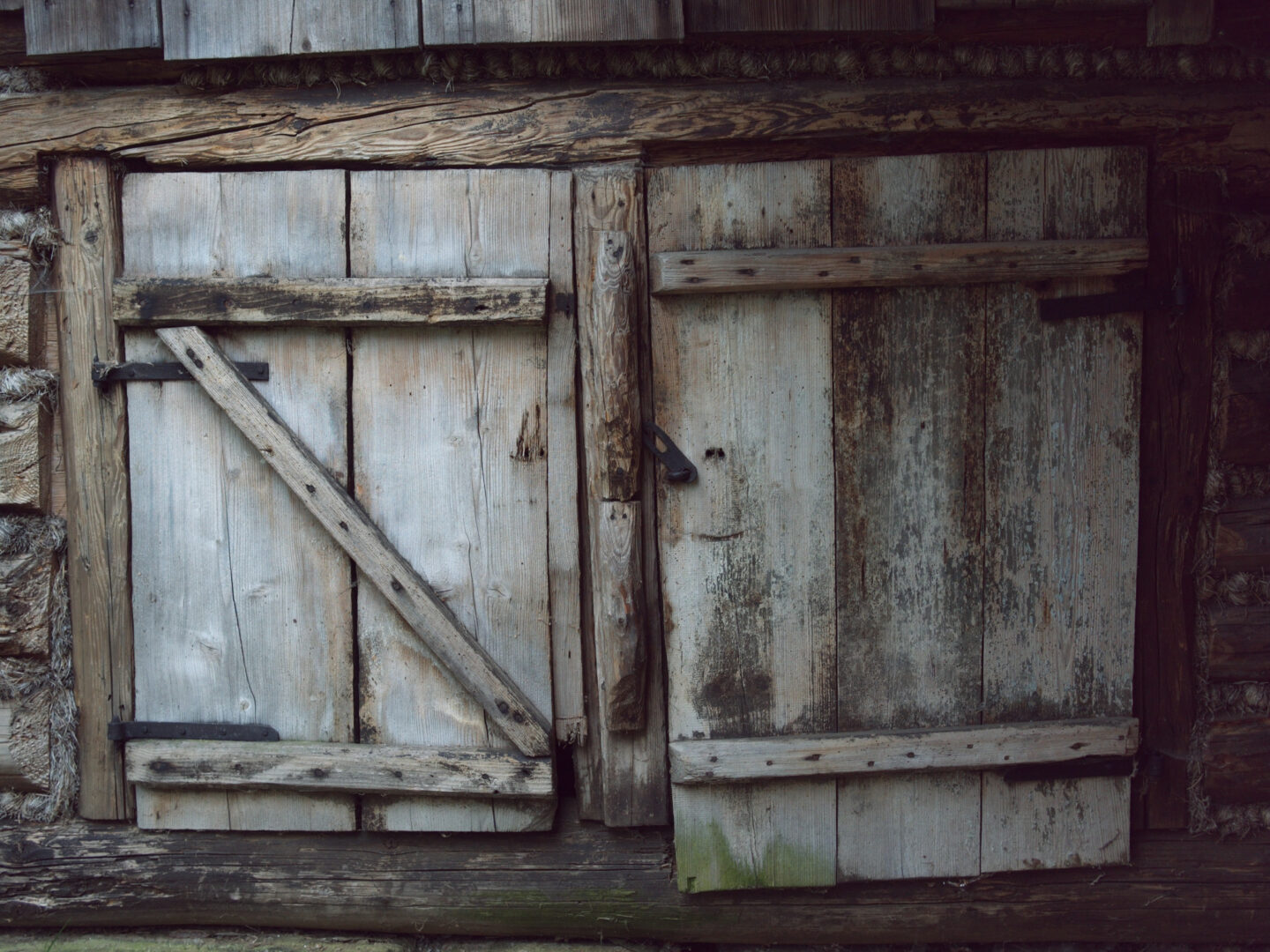 Weathered wooden double doors with a diagonal cross brace on the left door and black hinge hardware.