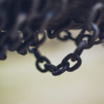 Close-up of rusty metal chains hanging from a dark wooden beam, with a soft blurred background.