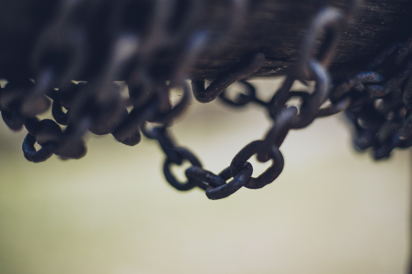 Close-up of rusty metal chains hanging from a dark wooden beam, with a soft blurred background.
