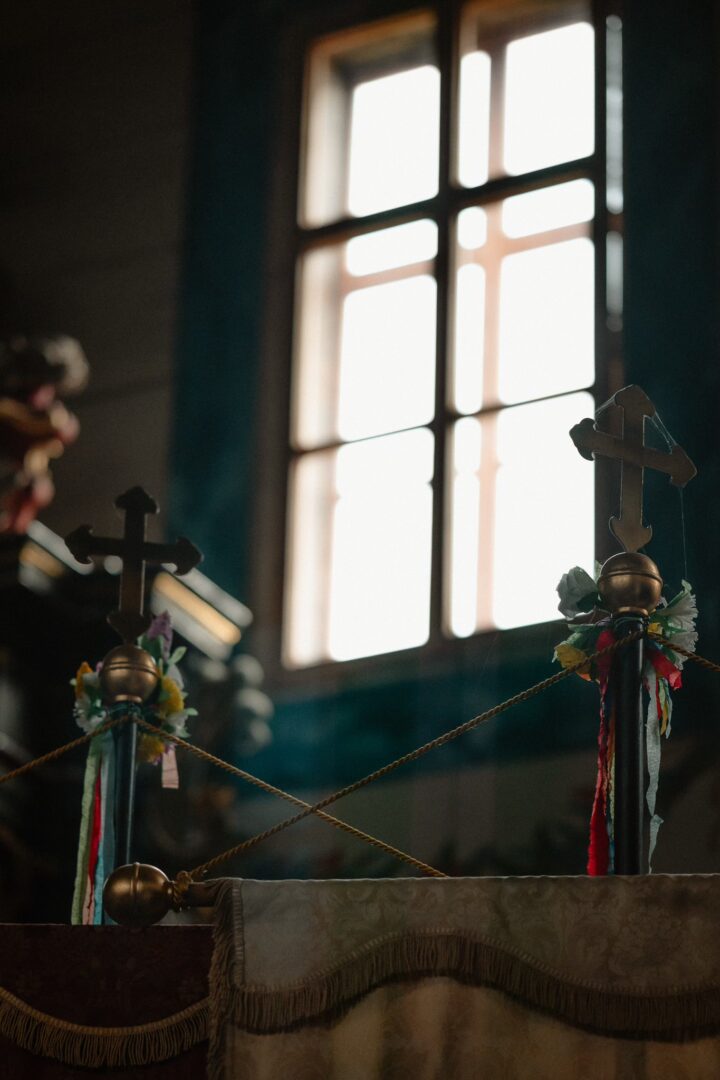Interior of a church altar with cross finials and colorful ribbons, lit by a bright window behind.