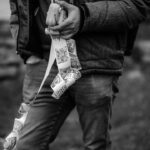 Person in a dark jacket holds a small white case while unrolling a long strip of black-and-white photos from it.