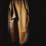 Golden-brown patterned robe with blue trim hanging on a hanger in a dark room.