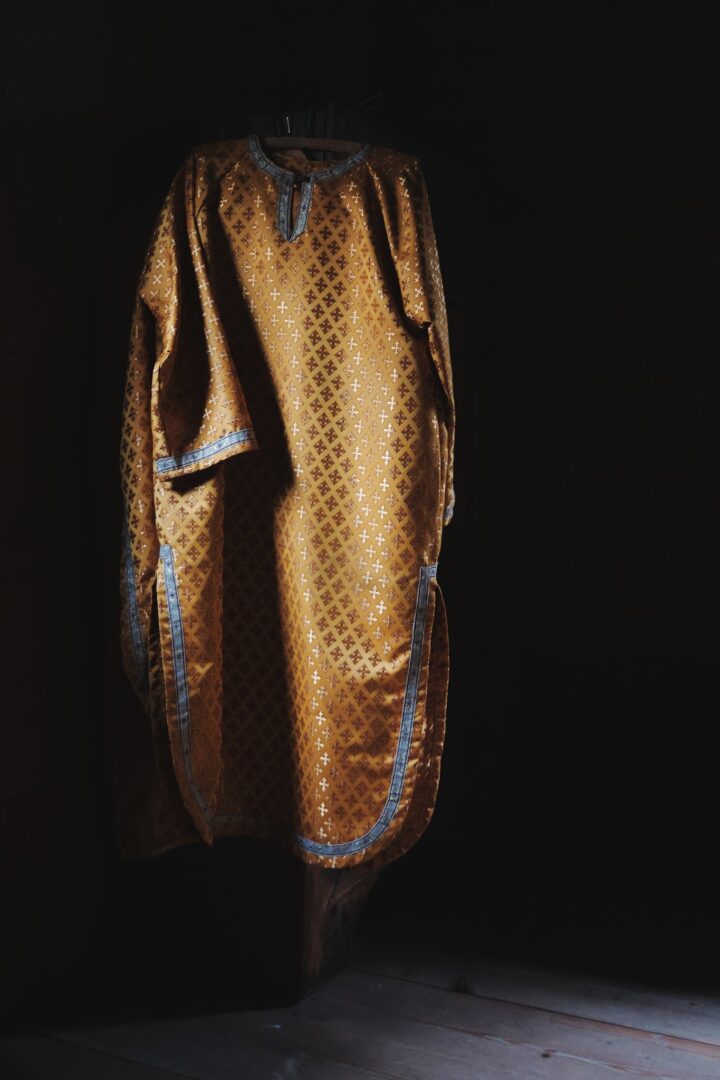 Golden-brown patterned robe with blue trim hanging on a hanger in a dark room.