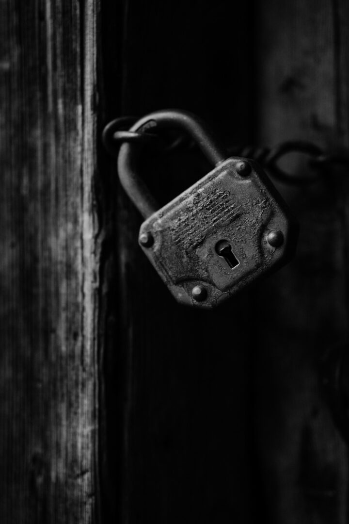 Close-up of a rusty padlock securing a weathered wooden door in black and white accuracy.