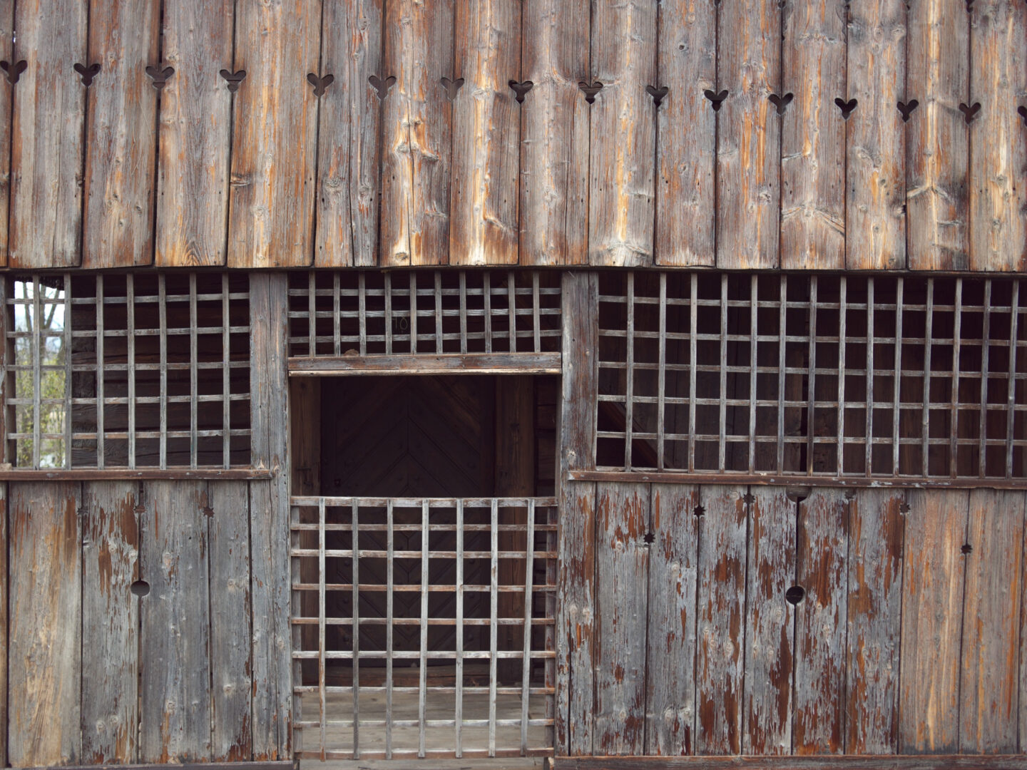 Weathered wooden facade with vertical planks, heart-shaped cutouts, and a central barred doorway like a rustic jail.