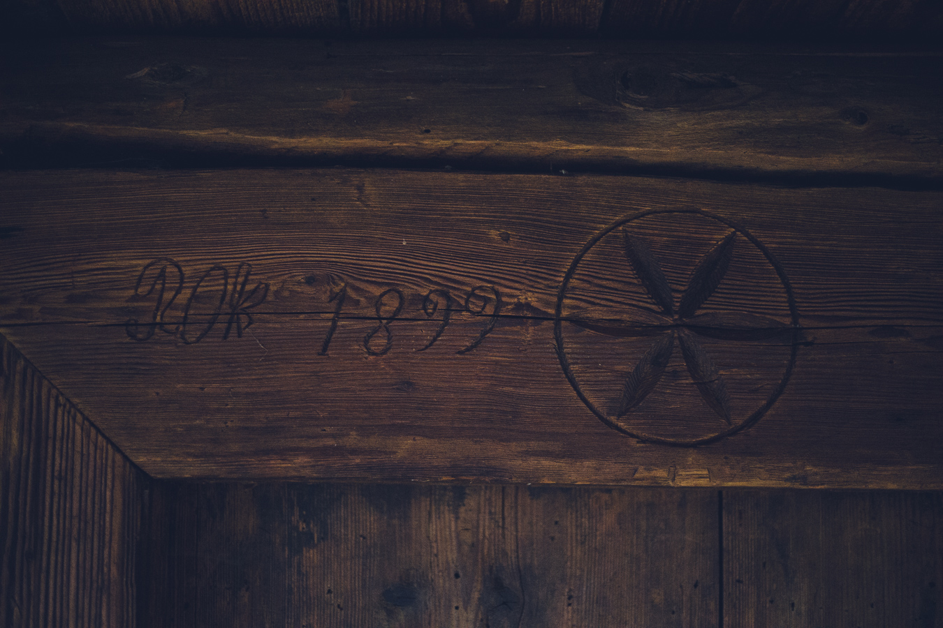 Carved circular emblem with an X-like four-pointed star inside on a dark, weathered wooden beam, with faded numbers to the left.