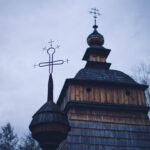 Wooden church with onion-shaped dome and spire, set against a cloudy sky with bare trees nearby