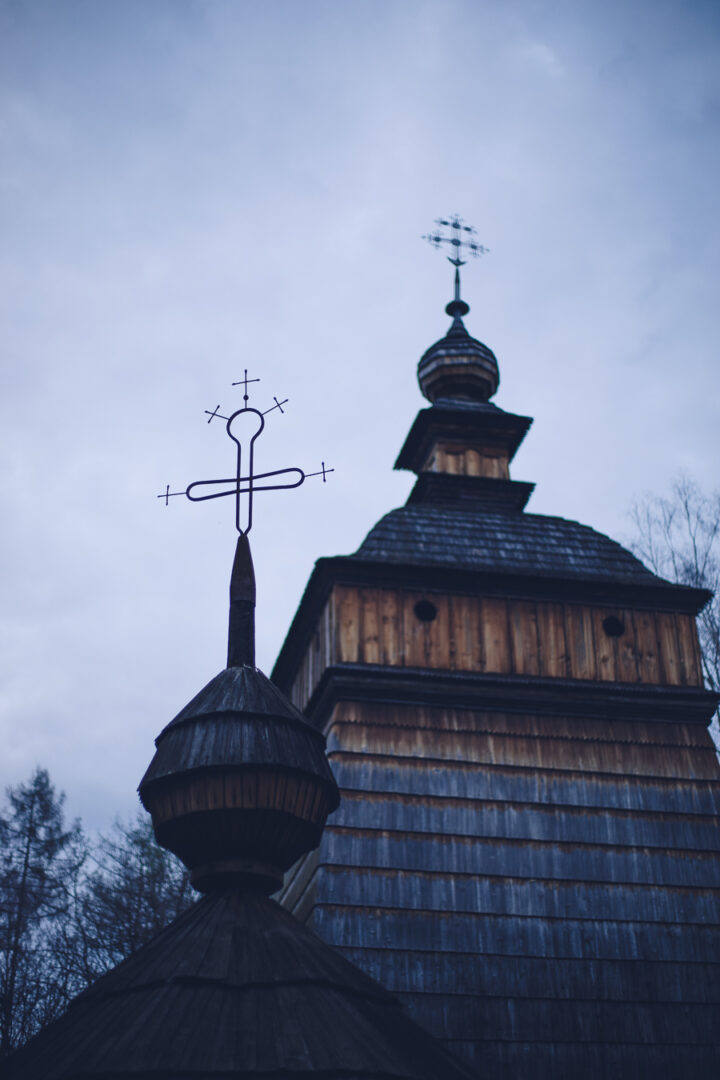 Wooden church with onion-shaped dome and spire, set against a cloudy sky with bare trees nearby