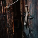 Old wooden door with a rusted latch and bar in a dim, narrow passageway behind it.