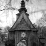 Black-and-white wooden church with a steep triangular roof, domed steeple, and a sunburst emblem on the front.