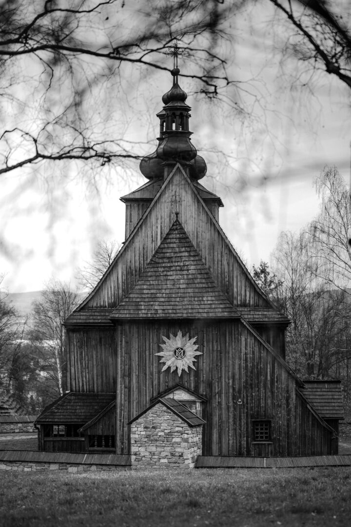Black-and-white wooden church with a steep triangular roof, domed steeple, and a sunburst emblem on the front.