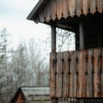 Weathered wooden cabin with carved balcony railing in a rural, leafless landscape.
