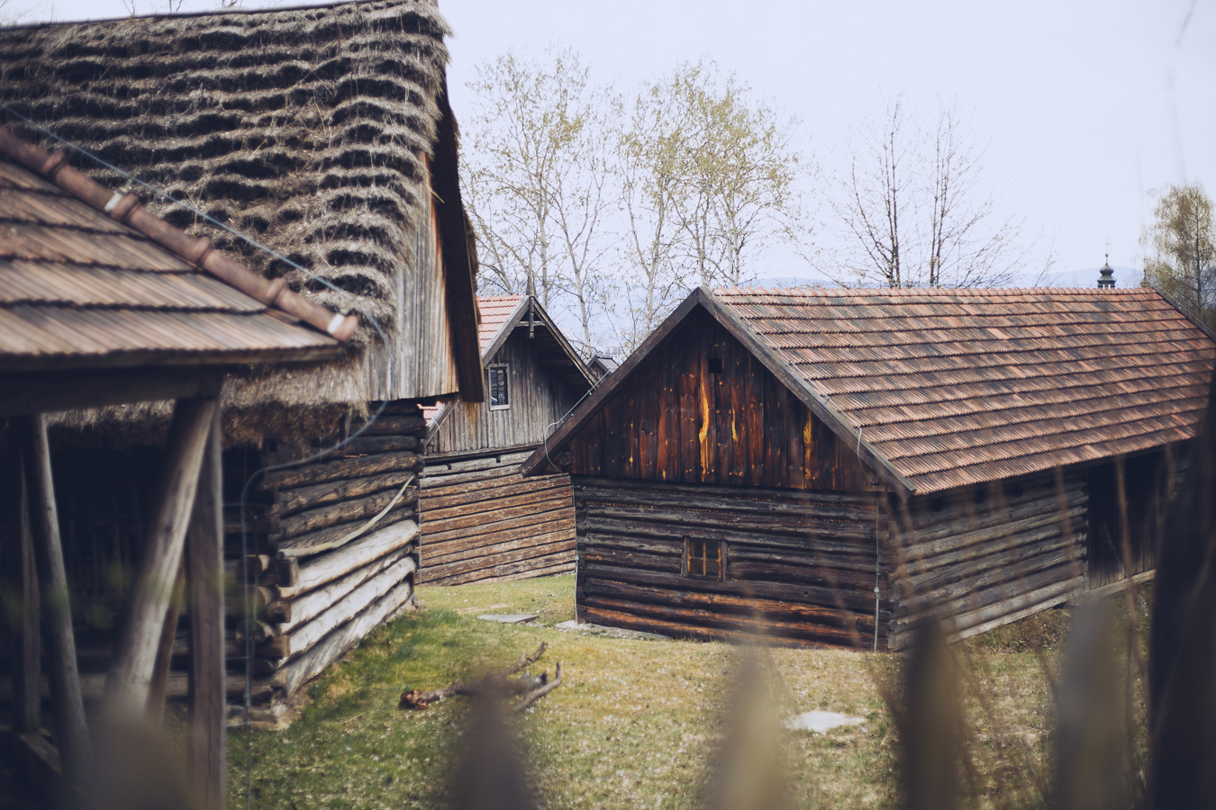 Row of rustic wooden houses with weathered logs and sloped roofs in a rural village setting.