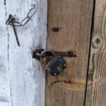 Rusty padlock and chain securing a weathered wooden door with peeling white paint on the left panel.