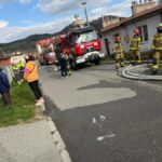 Firefighters in turnout gear with a red fire engine on a residential street, hoses laid out and onlookers nearby.