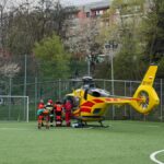 Emergency medical helicopter on a fenced football field, paramedics gathered near the craft ready to assist a patient.