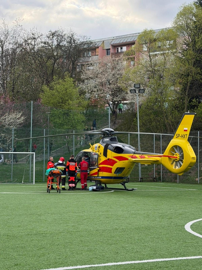 Emergency medical helicopter on a fenced football field, paramedics gathered near the craft ready to assist a patient.